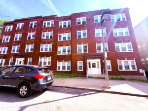 Exterior 54 Holworthy Street, four story brick building, white windows, parking on street.